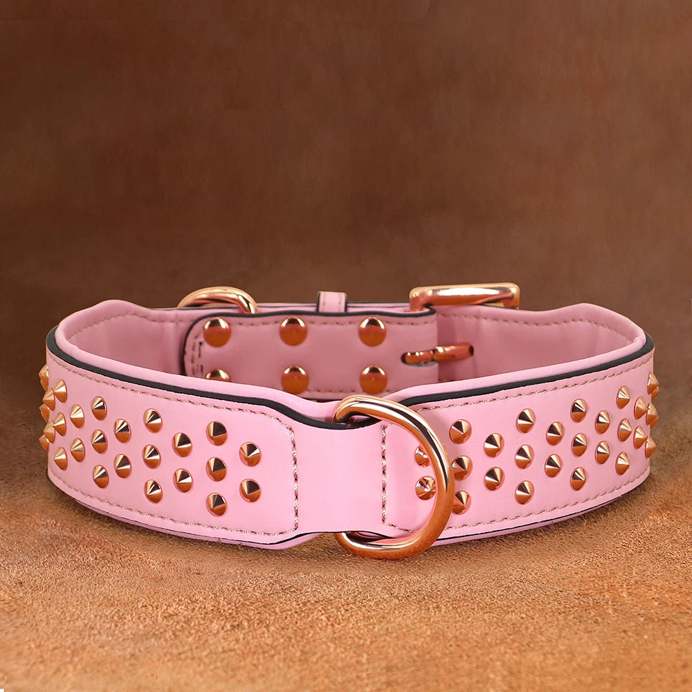 A pink leather dog collar with gold-toned hardware and metal spikes resting on a brown surface.