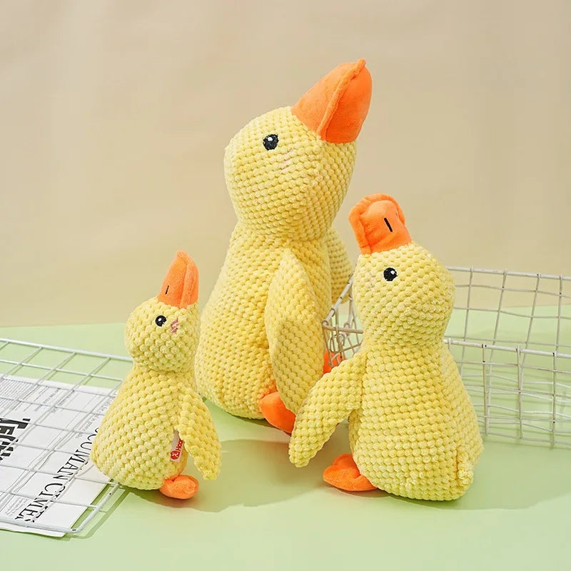 A yellow knitted plush toy of a duck with orange accents sitting next to a wire cage.
