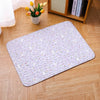 A rectangular white mat with a subtle floral pattern and non-slip base placed on a wooden floor.