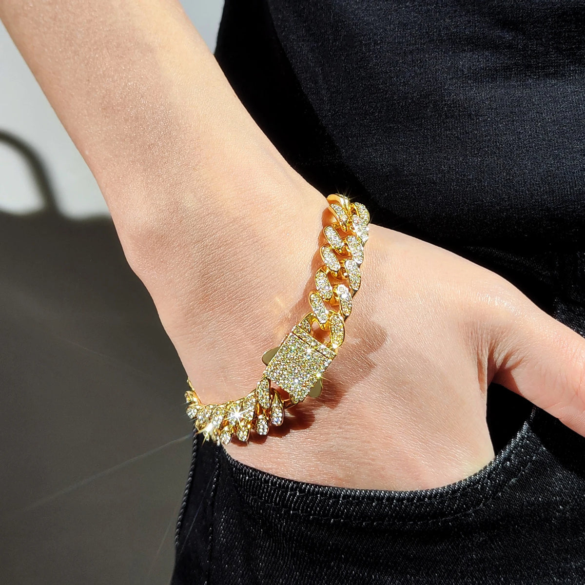 A close-up of a gold iced out Cuban link bracelet with rhinestone accents worn on a wrist.