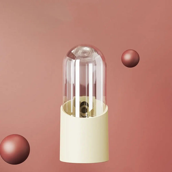 A clear glass bird water feeder with a light beige base and a small, spherical red component.