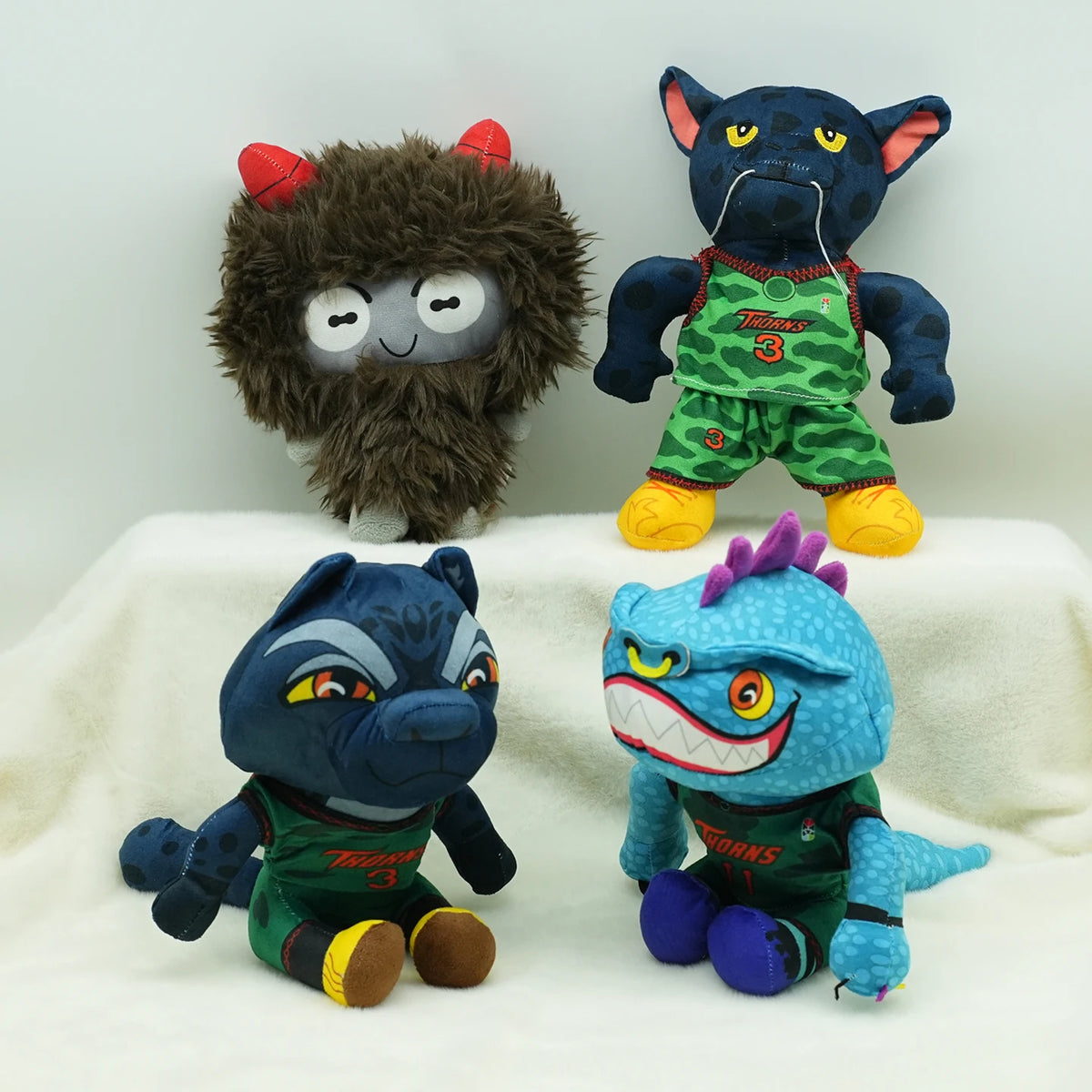A collection of three plush toys featuring cartoon animals including a dark blue cat, a black elephant, and a purple dragon.