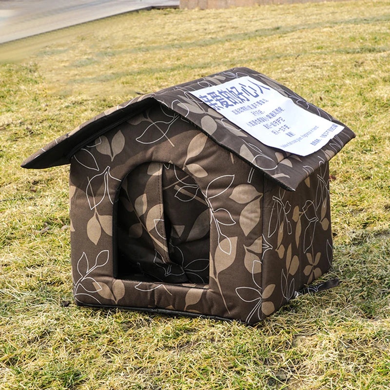 Maison pour chat extérieure marron et imperméable avec toit incliné, posée sur de l'herbe verte.