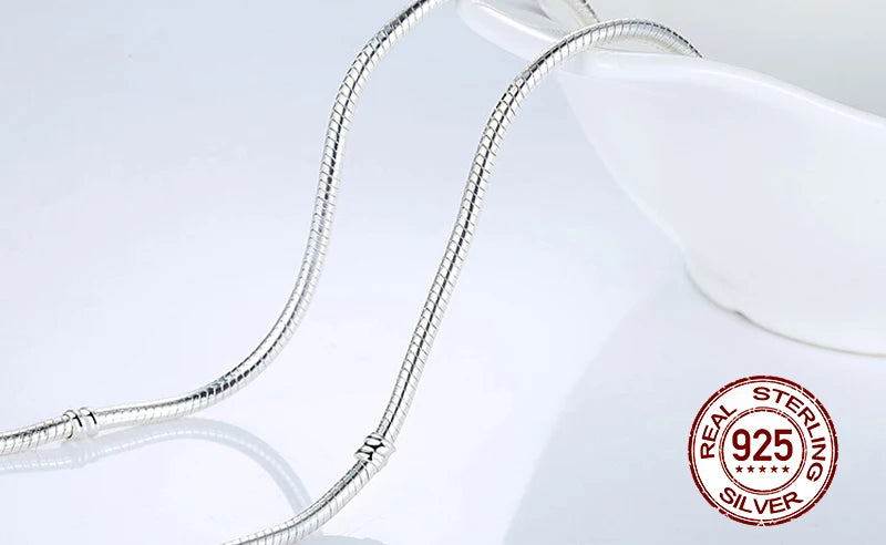 A silver sterling necklace featuring a snake chain and heart charm displayed on a white background.