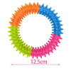 A circular ring toy made of colorful, spiky rubber teeth in orange, blue, and pink for dog chewing and play.