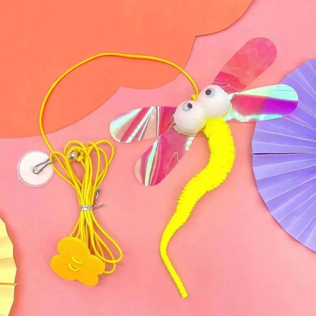 A yellow and pink interactive hanging cat toy with a rope and colorful wings is displayed on a pink background.