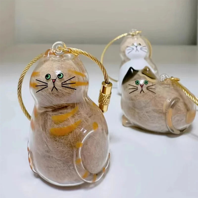 Ein Set aus zwei Katzen-Haaraufbewahrungs-Anhänger, eine hellbraune und eine weiße, aus klarem Harz.