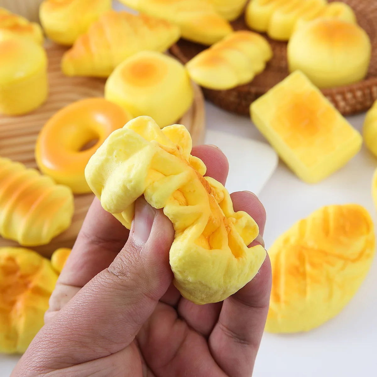 A hand holds a yellow squishy bread fidget toy with a textured surface, surrounded by other similar items.