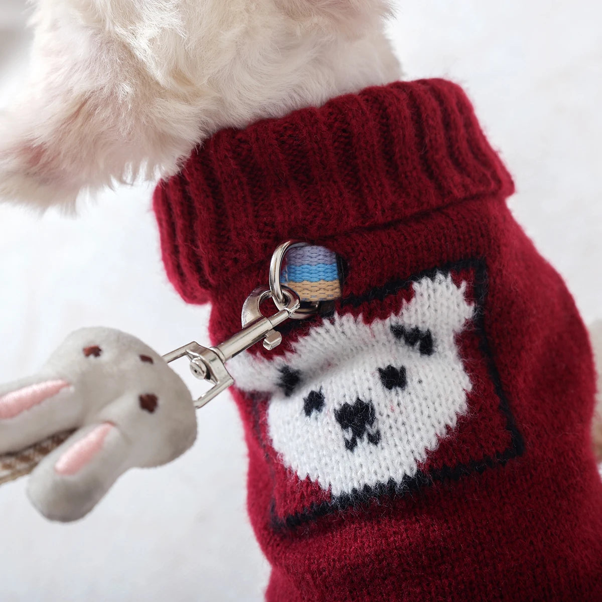 A close-up of a knitted red pet sweater with white paw print embroidery and a light pink fluffy collar.