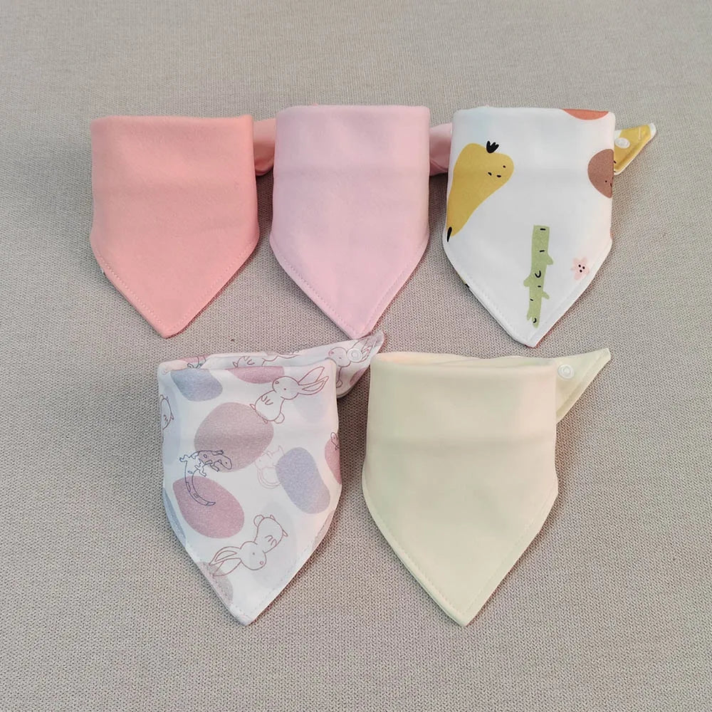 A set of five pink and yellow cotton triangle baby bibs with various cartoon prints laid out on a neutral background.