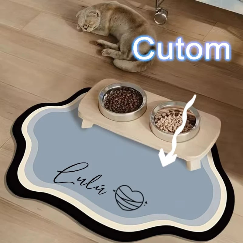 A light brown cat is resting on a pet feeding mat with a custom engraved name and food bowls.