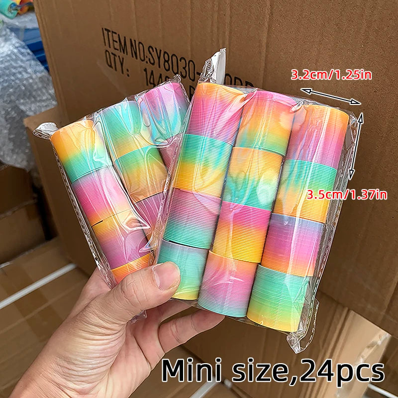 A hand holds a package of 24 mini rainbow coil toys in clear plastic packaging.