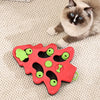 Un jouet distributeur de puzzles rouge avec des trous et des formes vertes est placé sur un tapis beige à côté d'un chat.