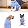 A dog wearing a blue patterned post-surgery recovery suit sitting on a white floor.