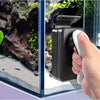 A hand is using a black and white magnetic aquarium cleaning brush to clean a glass tank.