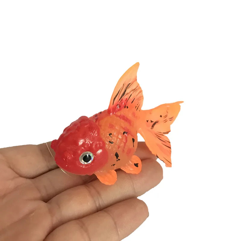 Ein kleines, leuchtendes, orange-rotes, leuchtstoffhaltiges Goldfisch-Dekor wird in der Hand einer Person gehalten.
