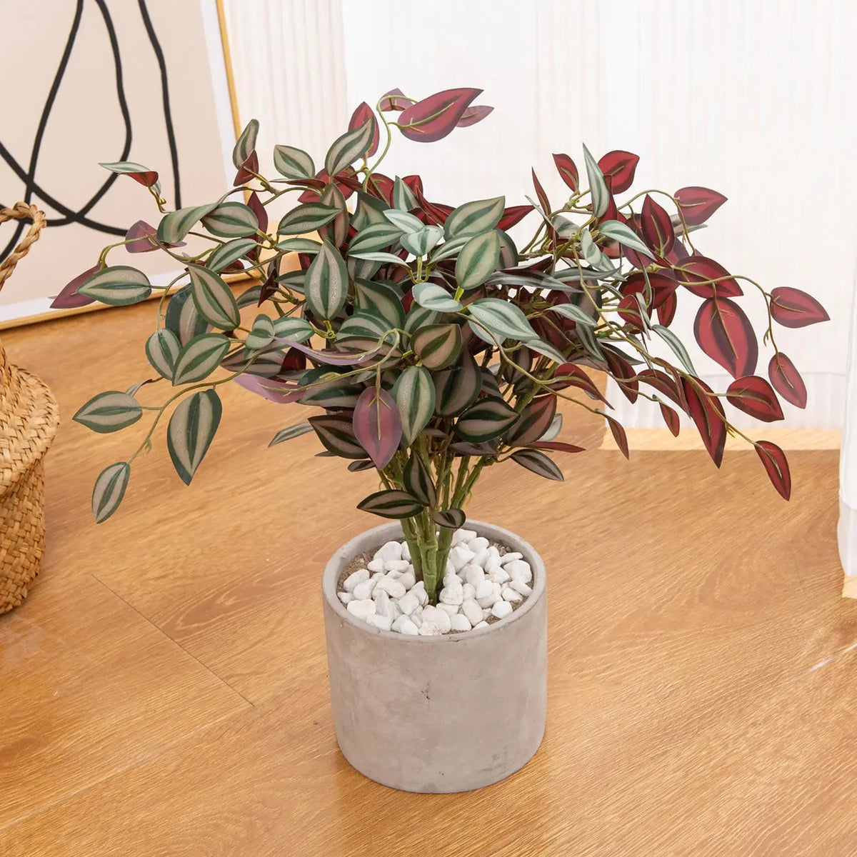 An artificial bonsai tree with variegated green and reddish leaves planted in a gray pot on a wooden floor.