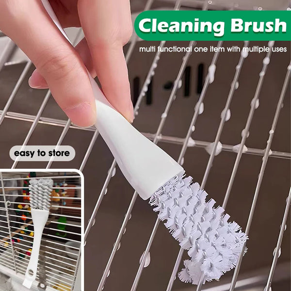 Une main tient une brosse nettoyante blanche à poils, positionnée sur la grille d'une cage de transport pour animaux.