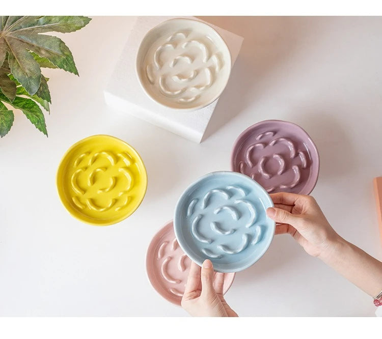 A collection of ceramic elevated bowls in yellow, pink, and blue are shown on a white surface.