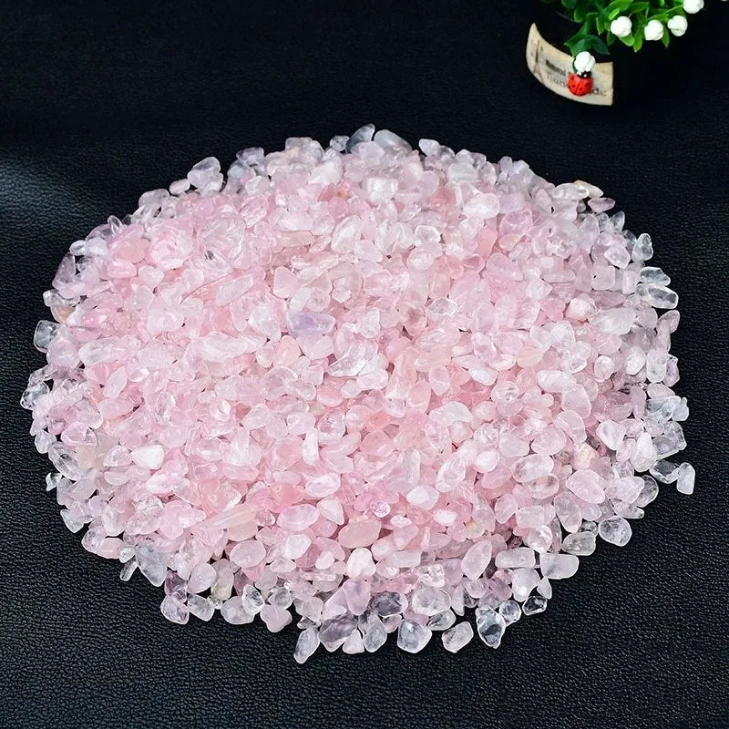 A pile of pink rose quartz crystal chips scattered on a dark surface.