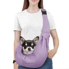 A woman is wearing a purple reversible hands-free dog sling carrier with a black strap and denim jeans.