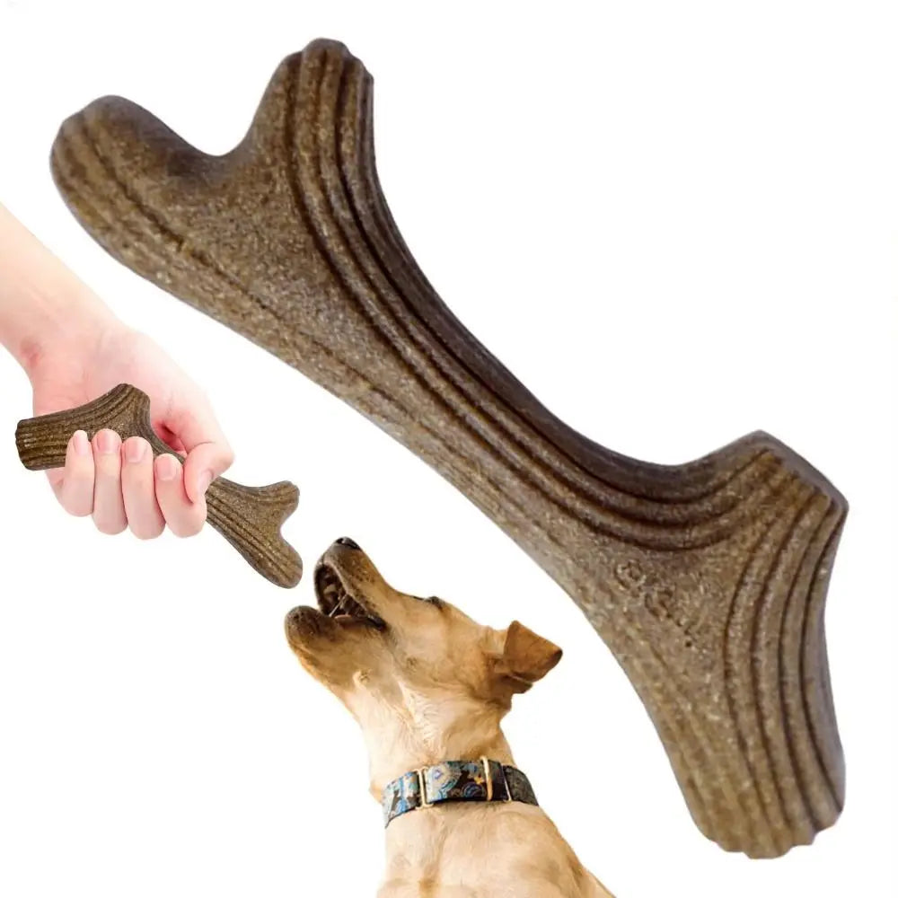 A hand holds a natural wood dog chew stick, showing its texture and shape against a dog's head.