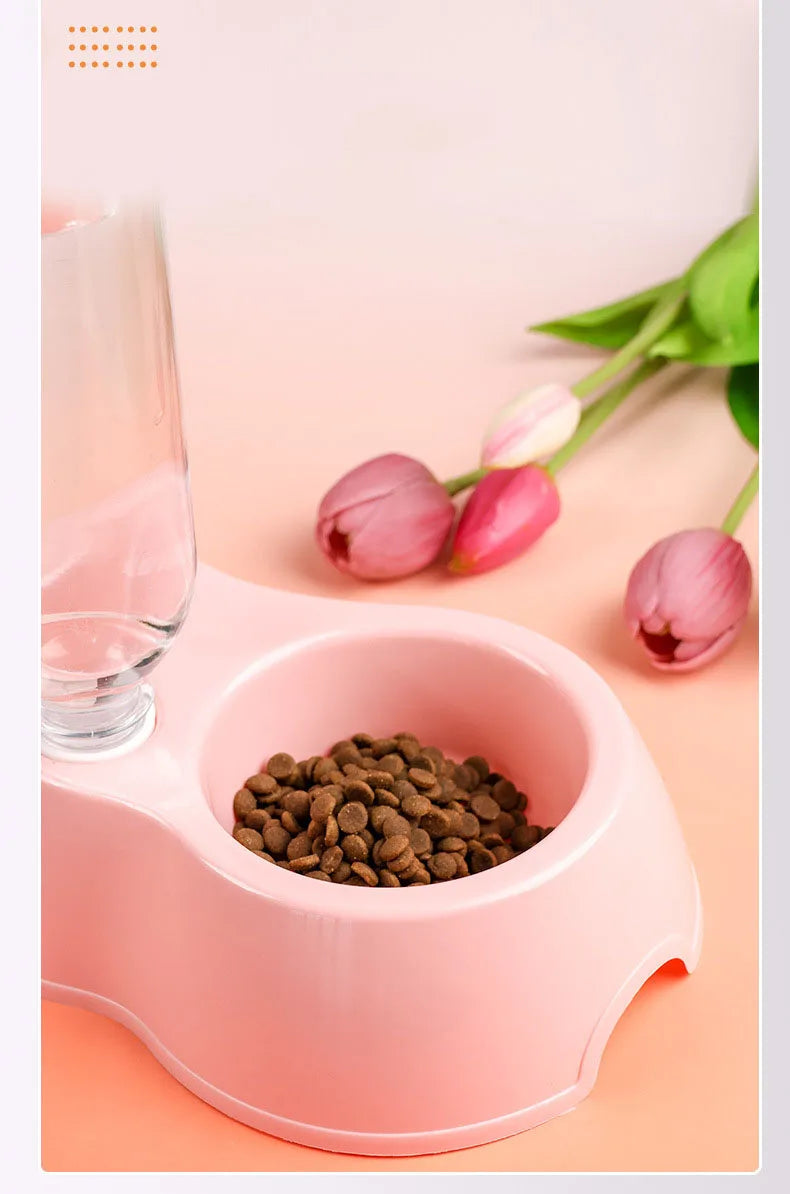 A pink dual-bowl feeder for cats and dogs is shown with kibble and water, next to a pink glass.