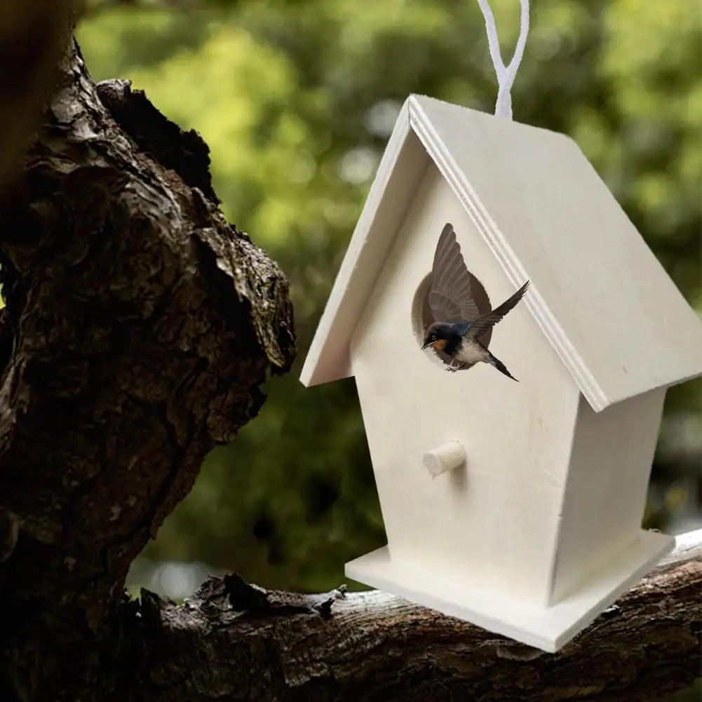 A white wooden wall-mounted bird house is attached to a tree branch, with a small bird visible inside.
