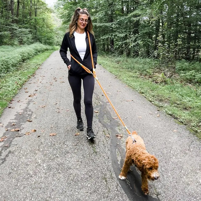A woman walks on a paved path with a hands-free dog leash attached to a fluffy dog.
