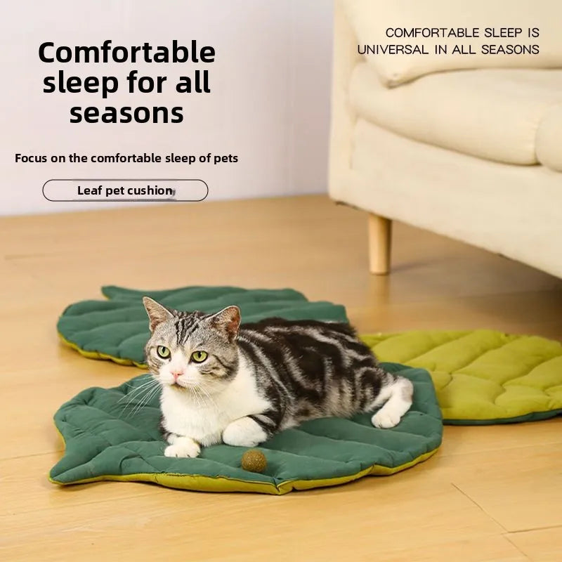 A tabby cat is resting on a green leaf-print pet cushion on a wooden floor.