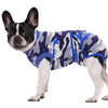 A black and white dog wearing a blue and gray camouflage pet recovery suit.
