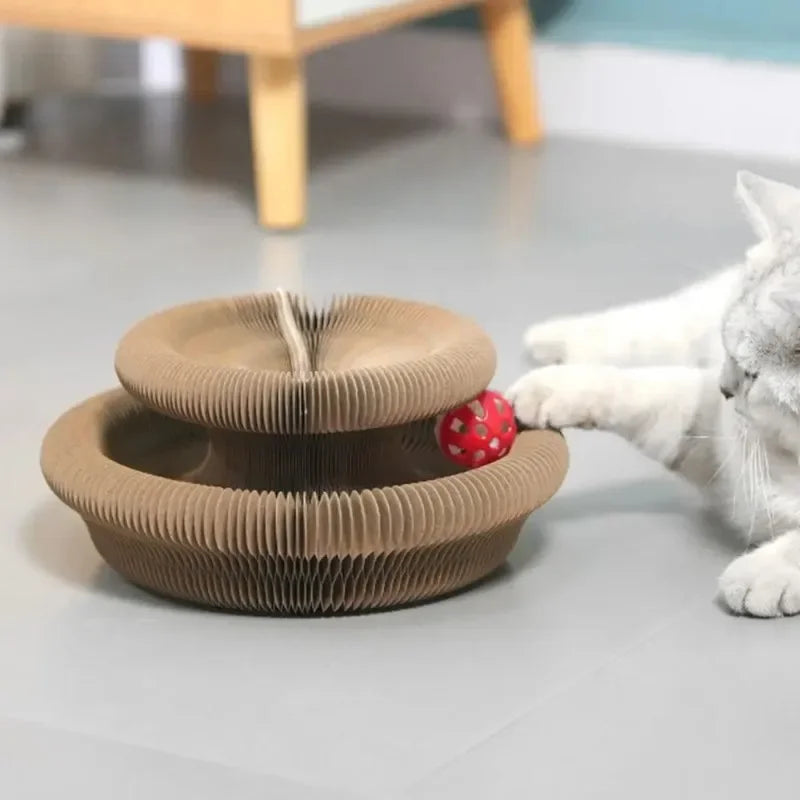 A beige accordion-style cat scratching board with an interactive red and white ball is shown next to a white cat.