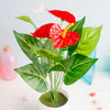 A vibrant red artificial anthurium plant with large green leaves displayed in a white pot.