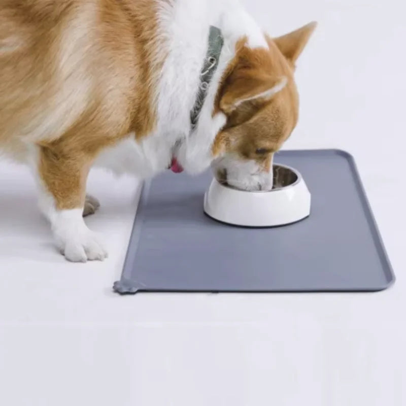 A dog is eating from a white feeding bowl placed on a gray waterproof silicone pet feeding mat.