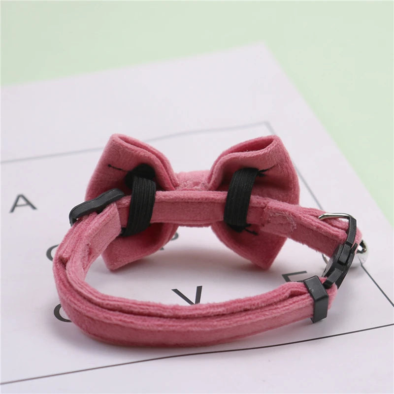 A pink plush velvet pet collar featuring a bow and bell, shown against a white background.