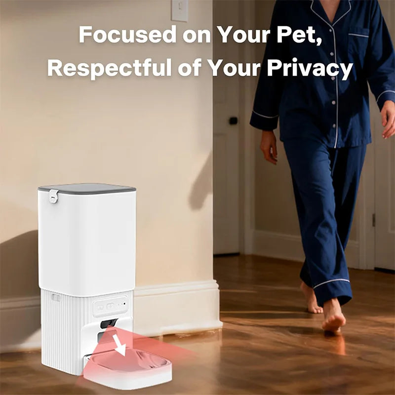 A white smart pet feeder device with a bowl is shown on a wooden floor next to a person.