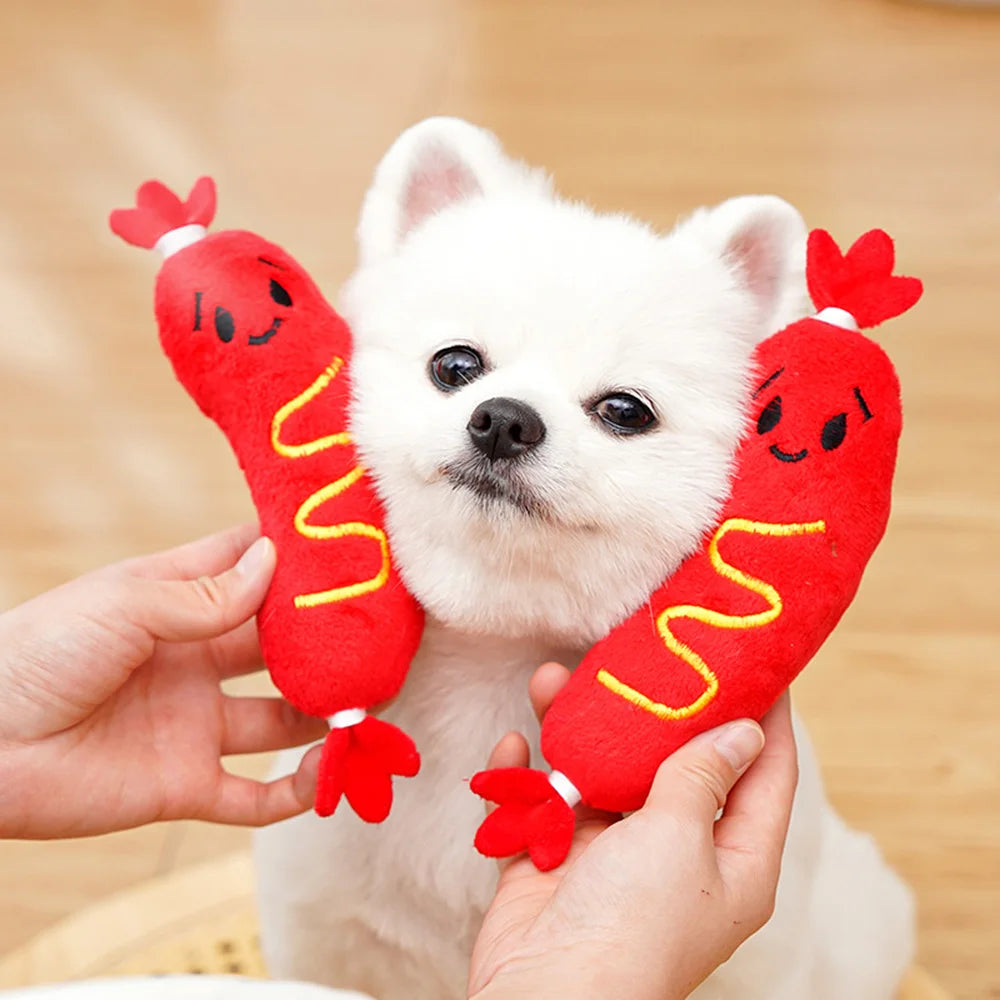 Un chien blanc tient un jouet à mâcher en forme de hot-dog rouge et qui fait du bruit.