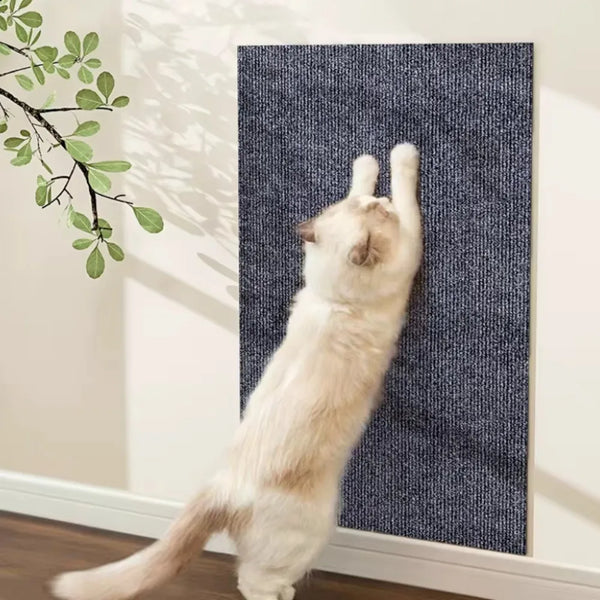 A light-colored cat is scratching against a dark blue textured mat mounted on a white wall.