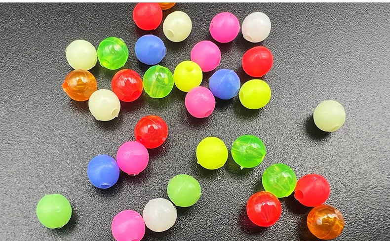 A collection of mixed glow-in-the-dark fishing beads in various colors like red, green, yellow, and purple scattered on a dar