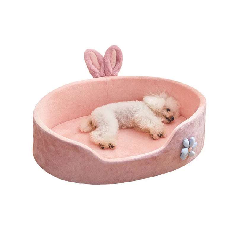 A pink plush pet bed with a removable cover and pink bunny ears, featuring a fluffy white dog lying inside.