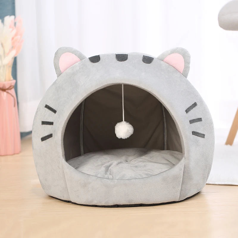 Lit de grotte en forme de chat gris avec des oreilles roses et des marques noires, doté d'un coussin amovible.