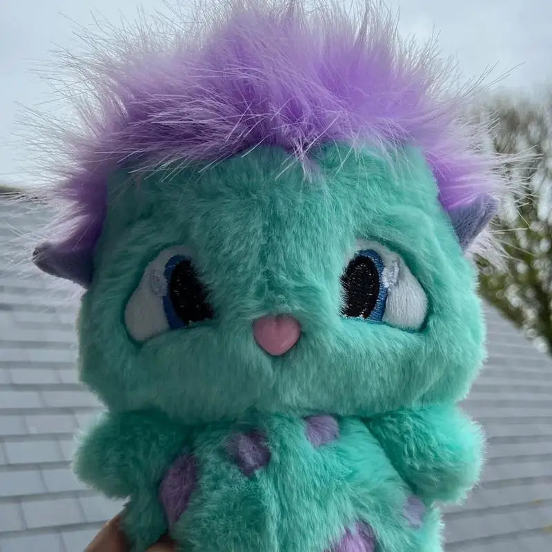 A cute teal and purple fluffy plush toy resembling a creature with large blue eyes.