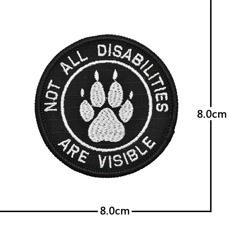 Black embroidered patch with white text and a paw print design stating Not All Disabilities Are Visible.