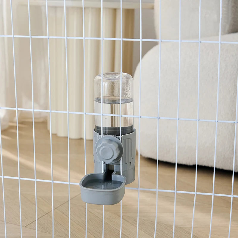 A clear automatic pet feeder waterer for dogs and cats is shown inside a wire mesh enclosure.