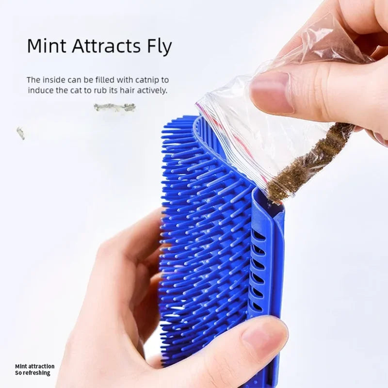 A hand holds a blue cat self-grooming massage comb with a corner mount, showing its bristles and a small amount of green mate