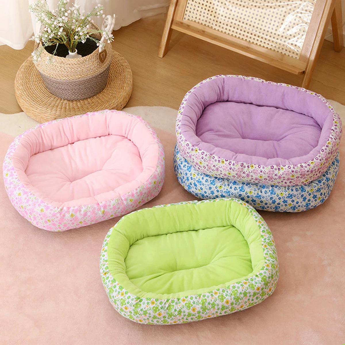 A set of three floral pet beds in pink, purple, and lime green fabric resting on a light pink surface.