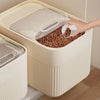 A hand is scooping pet food from an airtight storage container, which is a beige plastic box.