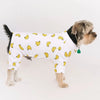 A dog wearing a white shirt with yellow corn designs, resembling pet pajamas.