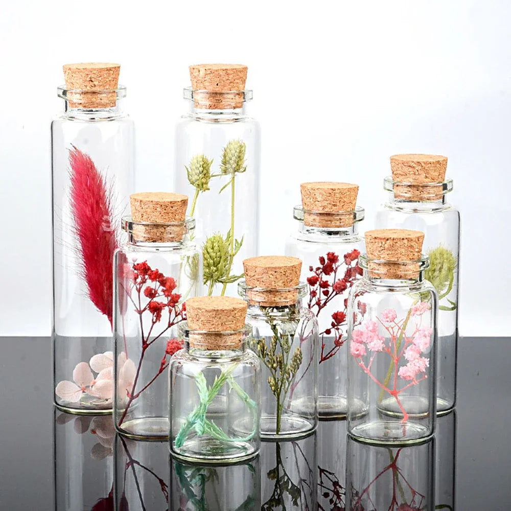 A collection of ten mini glass bottles with cork stoppers filled with various dried flowers and greenery.