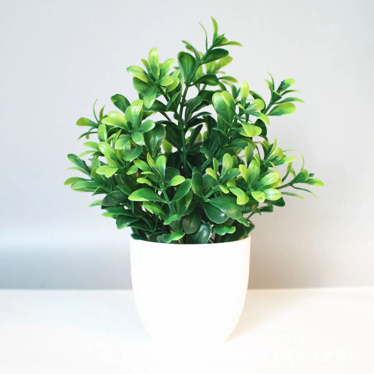 A vibrant green artificial bonsai plant in a white pot displayed on a light surface.